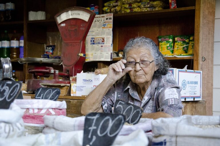 Marketplace Sydney. Senior vendor in a small store, managing goods with a scale and price tags