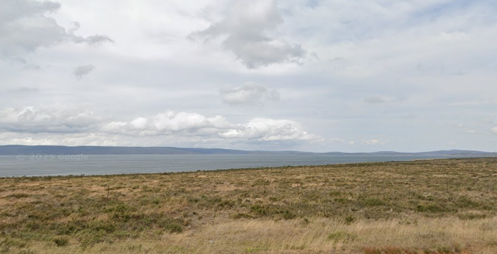 Liawenee view showing a serene field and the coastline, with hills visible on the horizon under a partly cloudy sky. Google map