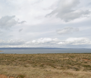 Liawenee landscape featuring a vast open field with the calm waters in the distance, under a cloudy sky. google map