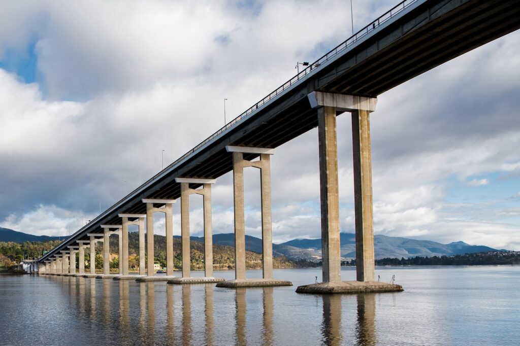 View of the Tasman Bridge from below, showcasing its concrete pillars and the calm river reflecting the structure. A scenic shot of the iconic Tasman Bridge in Tasmania