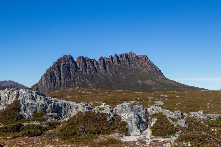 Cradle Mountain Peaks Under Clear Sky - Majestic peaks of Cradle Mountain towering against a vibrant blue sky, showcasing rugged rocks and scenic surroundings