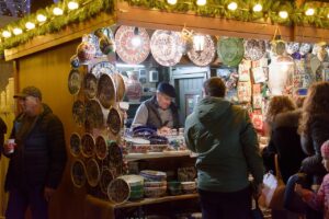 Shoppers at a craft fair browsing unique handmade ceramics and pottery at a market stall, illuminated by warm lights